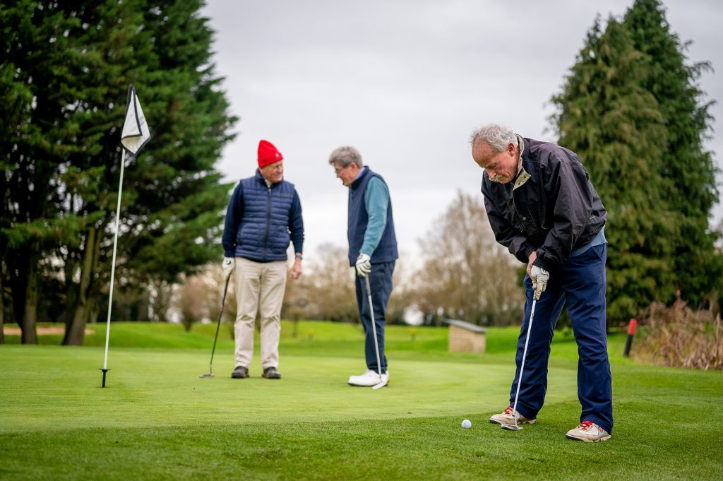 three men playing golf on an overcast day with trees